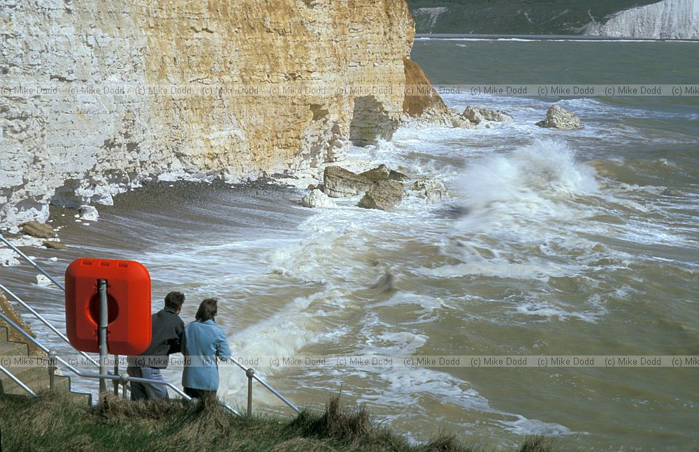 Couple overlooking waves and white cliffs Cuckmere haven
